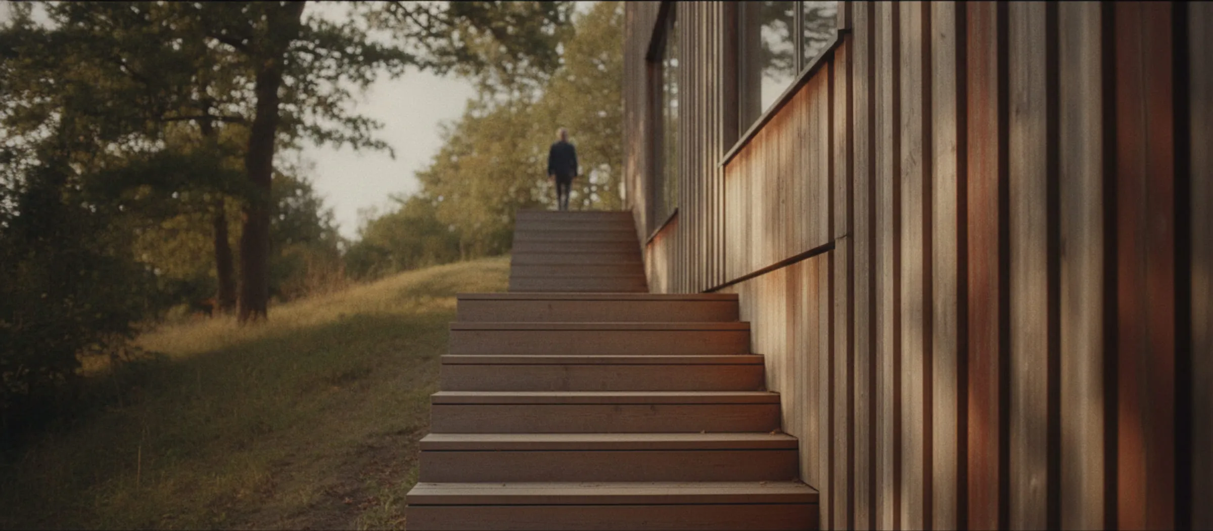 Træbeklædt facade på en skrånende grund med en trætrappe op fra vejen.