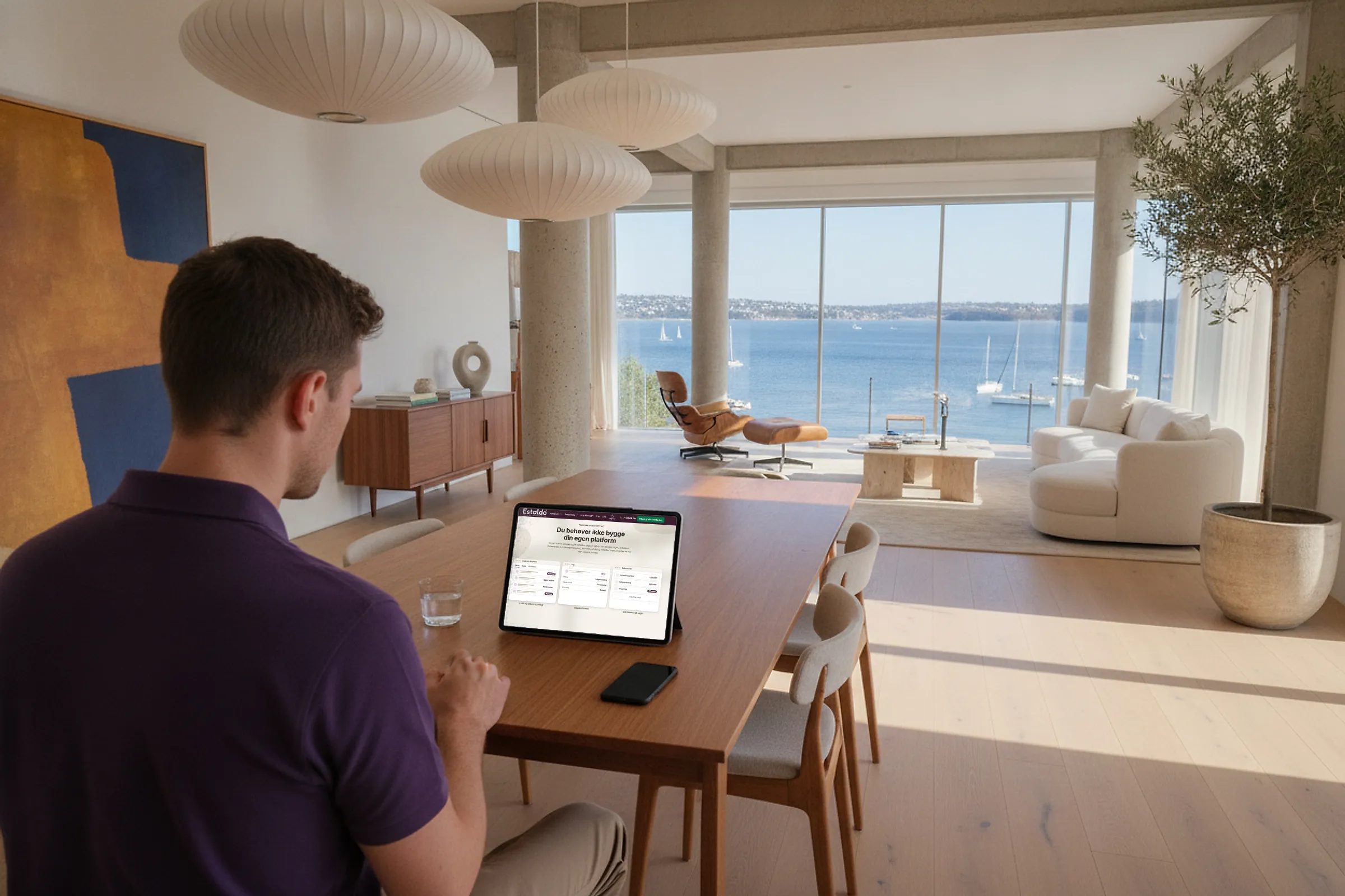 Partner sidder ved et spisebord i en moderne, lys lejlighed med havudsigt og kigger på en tablet med Estaldos platform.